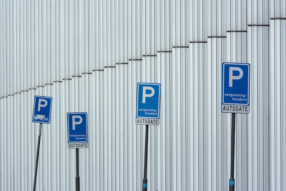 Four blue parking permit signs mounted on black metal posts are positioned in front of a large, vertically ribbed metallic wall. The signs display a white 'P' symbol, with the words 'vergunninghouders' and 'AUTODATE' beneath, indicating parking restrictions for permit holders. The signs are evenly spaced from left to right, with some signs tilting slightly. The background features the textured metal surface illuminated by natural daylight, with no vehicles or other objects visible in the scene. The image relates to parking regulations, relevant in the context of house removals and moving services provided by Hounslow Man and Van, emphasizing compliance with street parking permit rules during a home relocation process.